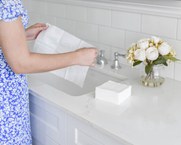 Easydry white small towel or hand towel. It is shown here being used to dry someones hands and is pictured in a bathroom or spa setting with a vase of flowers.