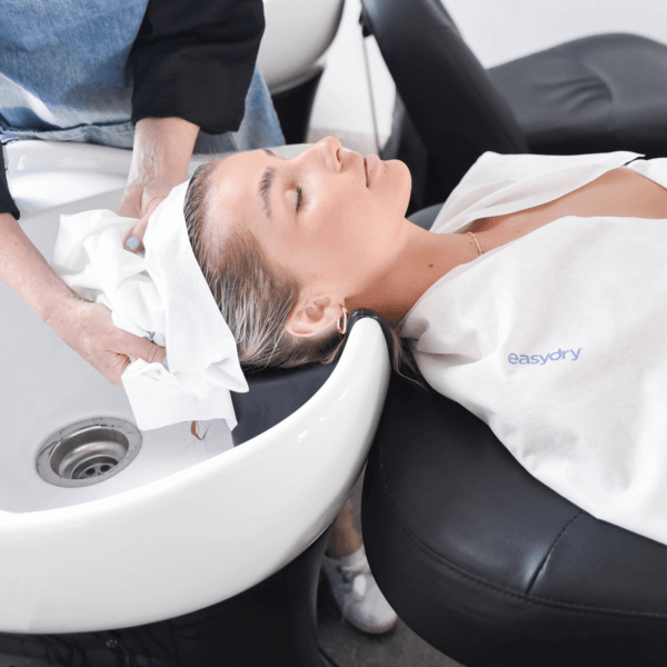 Easydry white medium disposable towel shown as a towel being wrapped into a turban on a clients hair and as a towel on the clients shoulders.